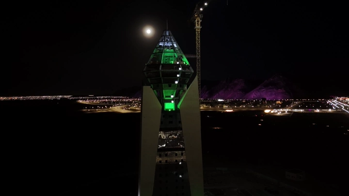 برج الجوهرة في حائل ليلاً مع رافعة وجبال في الخلفية، لقطة جوية.