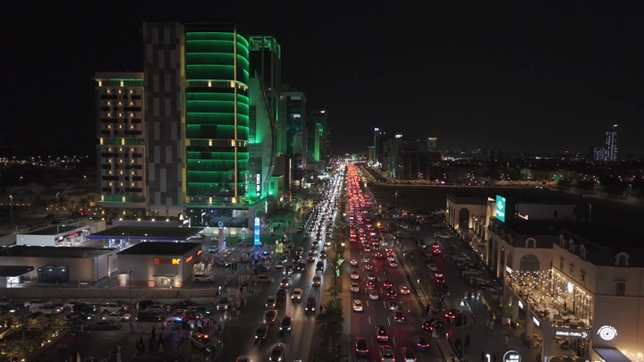 مباني مضاءة باللون الأخضر مع شوارع مزدحمة في مدينة الخبر ليلاً، تصوير درون ليلي.