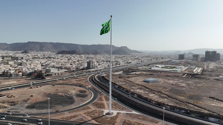 علم السعودية يرفرف فوق مدينة في النهار، تصوير جوي درون.