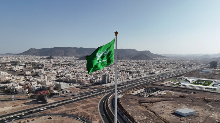 علم السعودية يرفرف فوق مدينة وجبال، تصوير جوي درون.